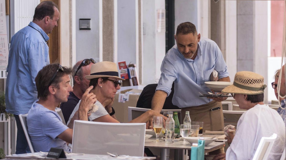 Un camarero sirve varias bebidas en una terraza a un grupo de clientes.