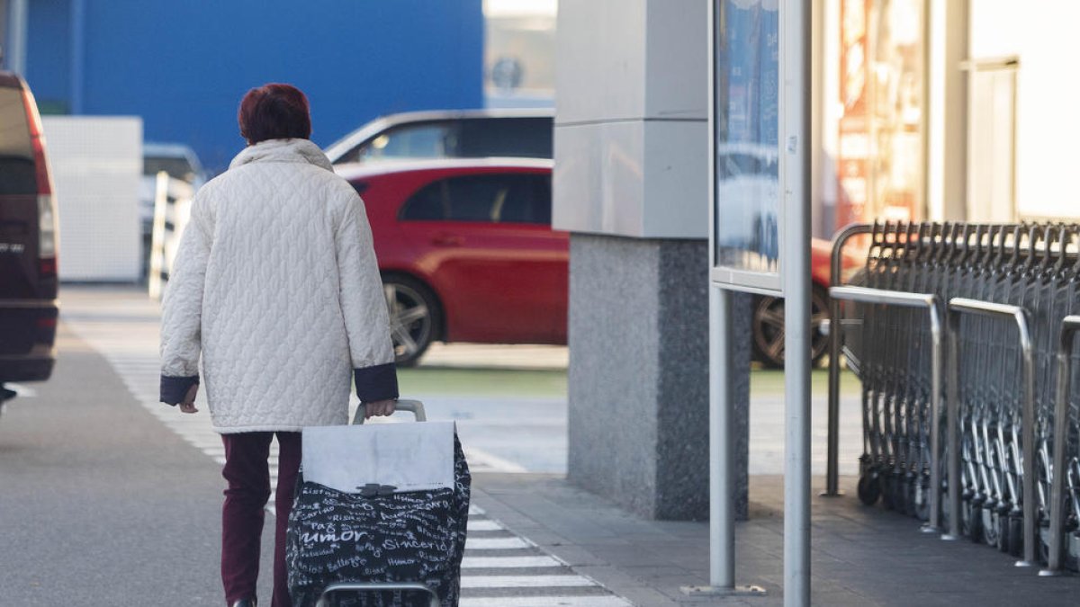 Una mujer sale de un supermercado con el carro de la compra.