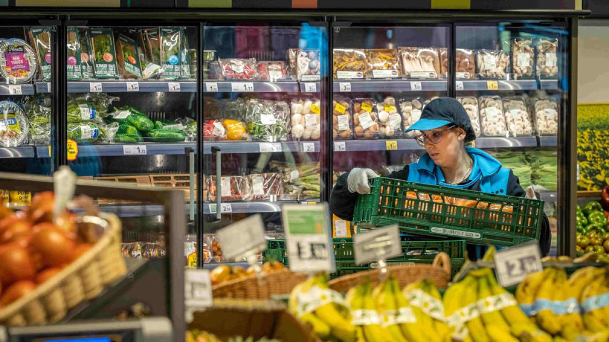 Una treballadora reposant fruita en un supermercat.