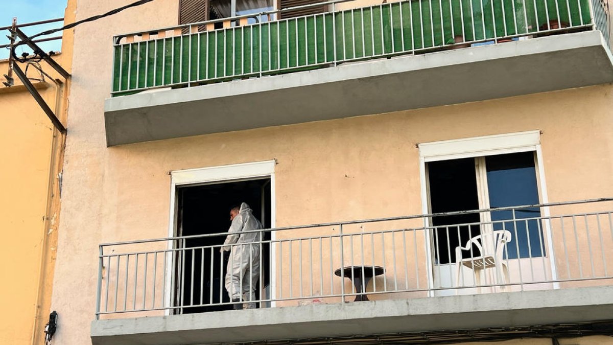 Un agente de la policía científica sale del balcón del piso incendiado en Figueres en la investigación de las causas del fuego.