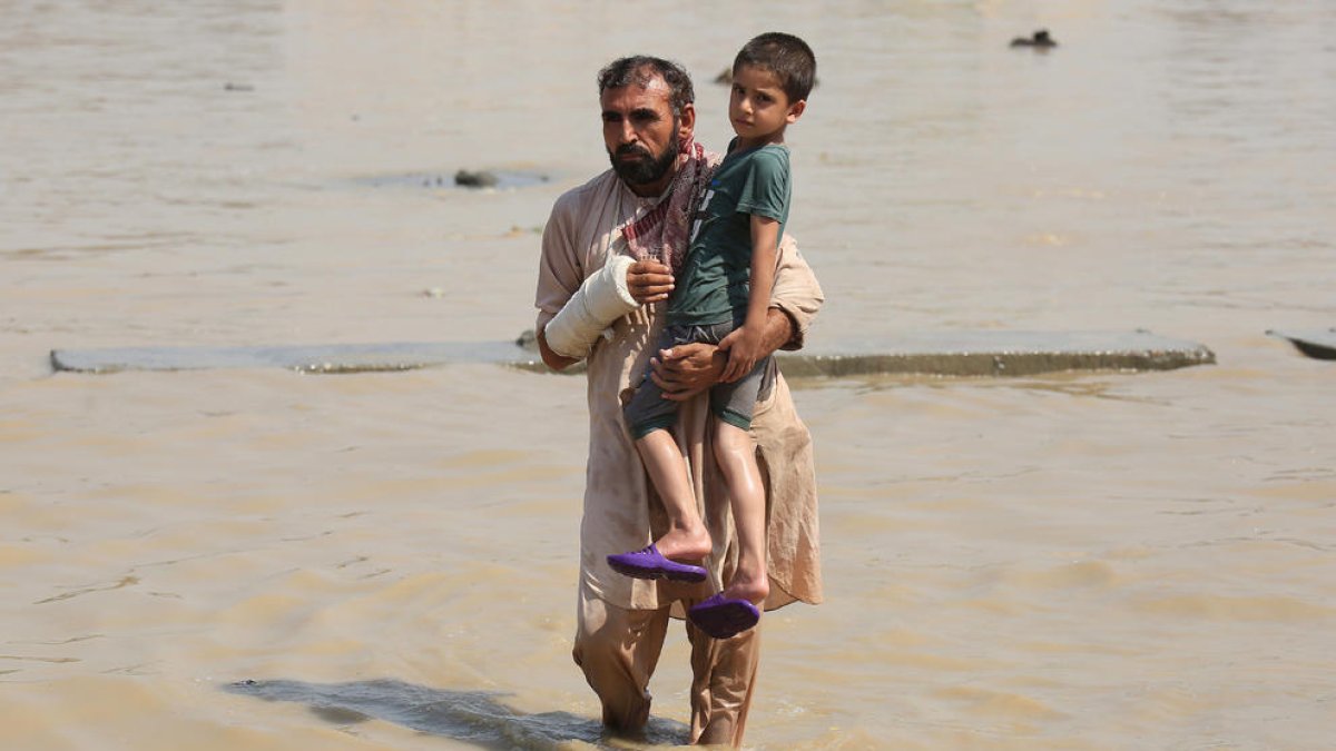 Un hombre sostiene a un niño en una zona inundada.