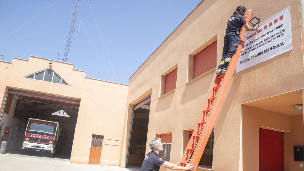 Dos bomberos voluntarios colgando ayer la pancarta en el parque de Agramunt. 