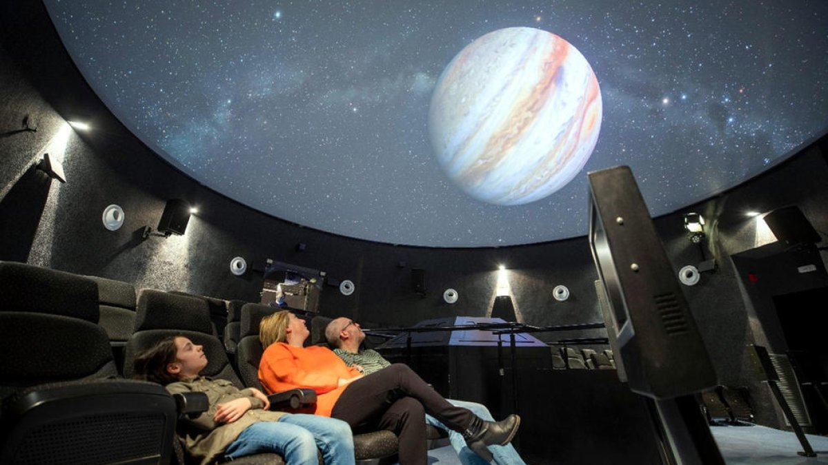 Tres visitants gaudeixen de la projecció d'una pel·lícula al planetari del Parc Astronòmic del Montsec (PAM) d'Àger.