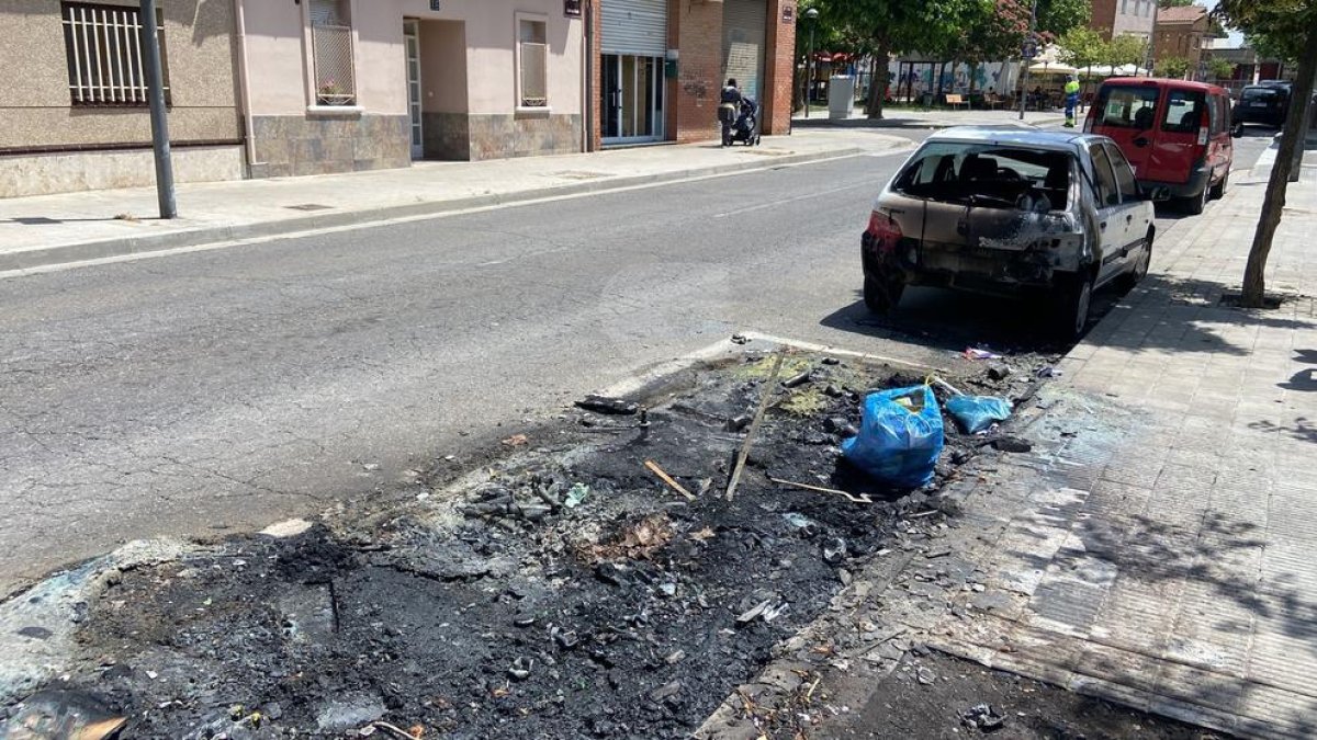 Les restes del contenidor cremat i el vehicle afectat pel foc al carrer Antoni Solé de Lleida.