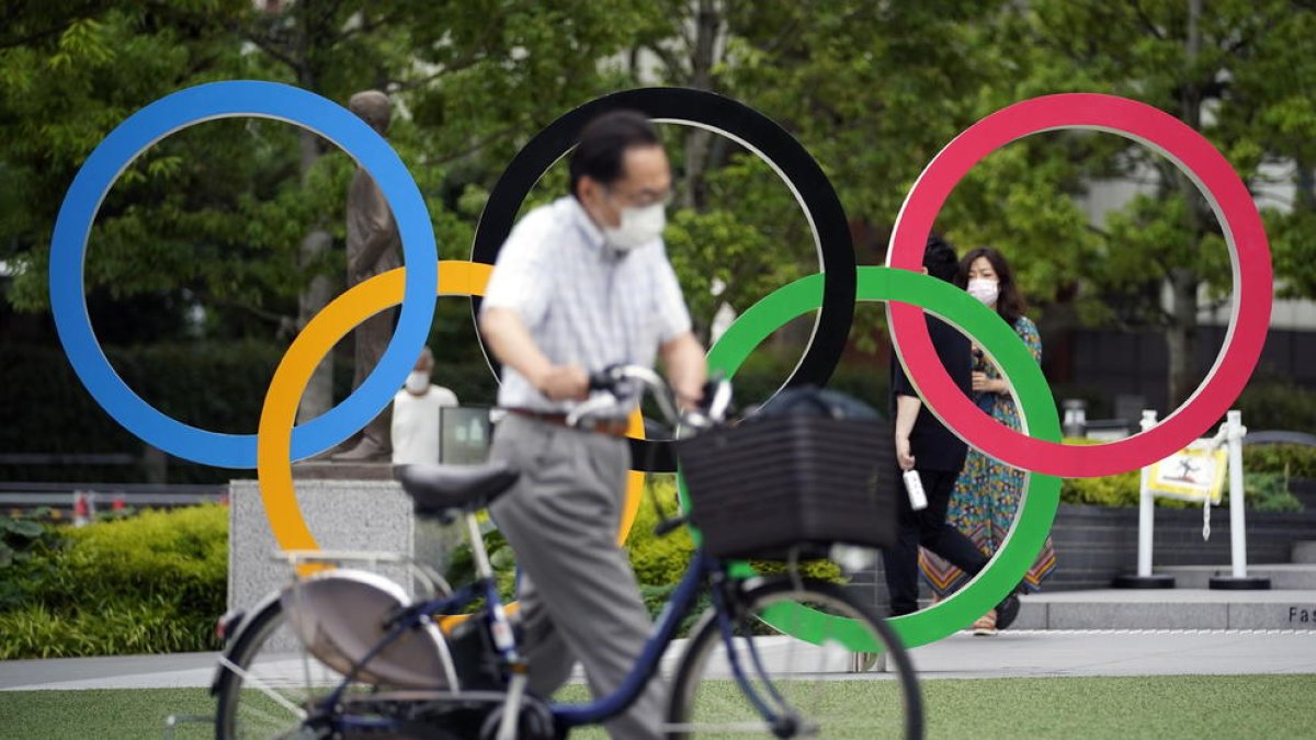 Un ciudadano de Tokio camina con su bicicleta delante de unos grandes aros olímpicos.