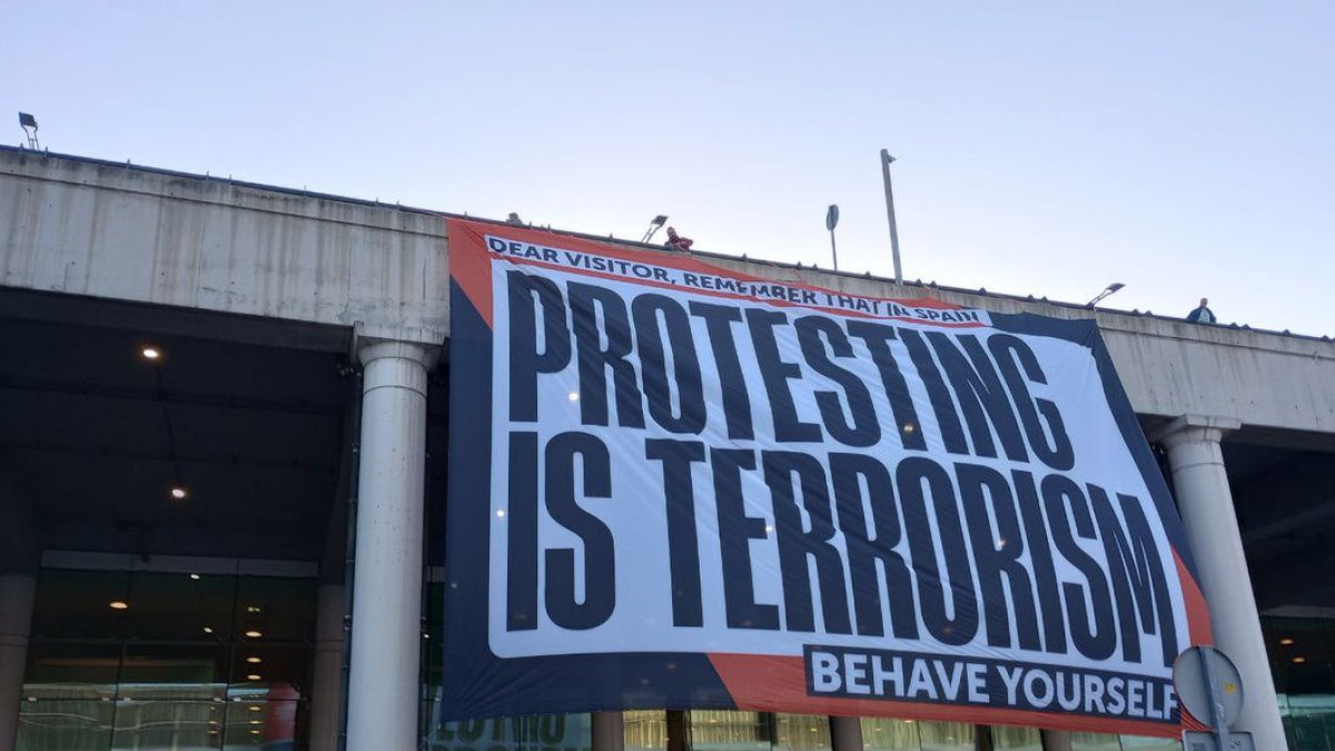 Òmnium va penjar una lona a l’aeroport del Prat amb el lema “a Espanya protestar és terrorisme”.