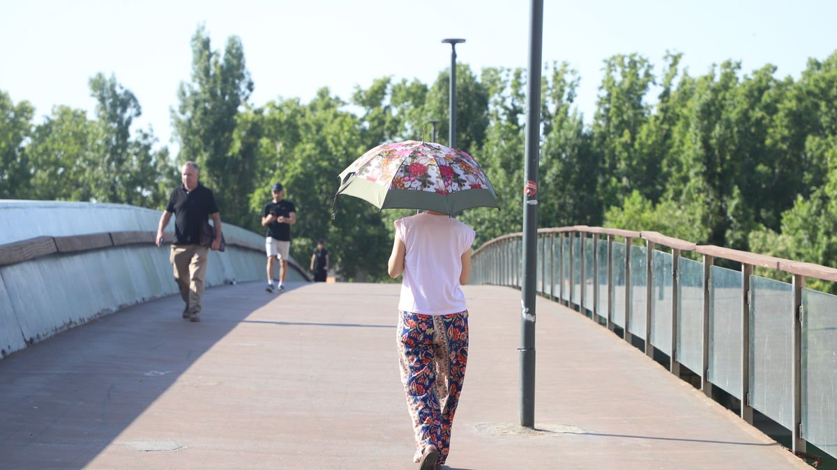 Una dona creuant ahir la passarel·la dels Camps Elisis amb un paraigua per protegir-se del sol.