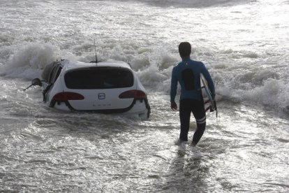 Un surfista passa davant d’un cotxe a la platja de Vilassar de Mar.