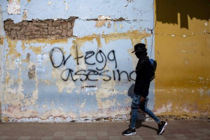 Un joven con la cara tapada camina delante de una pintada en Nicaragua.