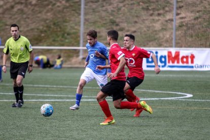 Un jugador del Lleida Esportiu B pugna pel control de l’esfèrica davant de dos rivals sota l’atenta mirada del col·legiat.