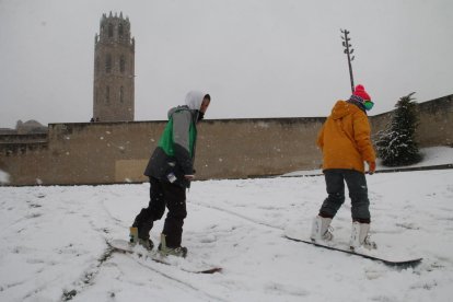 Dos jóvenes con tablas de snowboard intentando esquiar en los aldeaños de la Seu Vella. 