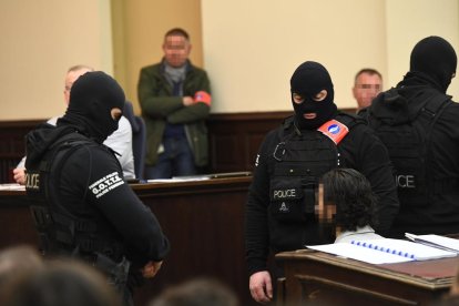 Agentes de policía enmascarados custodian en el tribunal a Salah Abdeslam, cuya cara está pixelada.