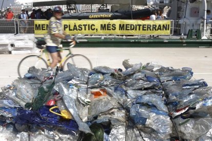 Un vaixell de l'organització Greenpeace al port de València davant d'un munt de bosses de plàstic.