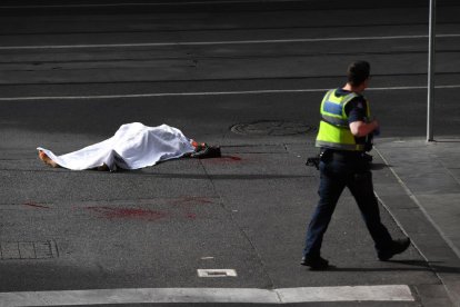 El cadáver de la víctima, en el suelo, custodiado por un policía.