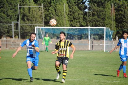 Un jugador de cada conjunto disputan el balón, que está a punto de caer al suelo.