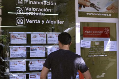 Un client mira les ofertes de pisos a la venda a l’aparador d’una immobiliària.