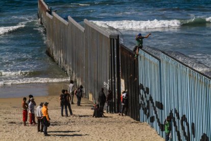 Imagen de la frontera sur de Estados Unidos con inmigrantes en el muro que parte ambos países.