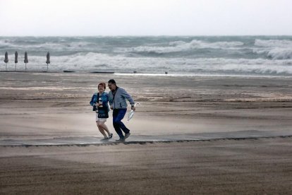 Una pareja frente al gran oleaje de una playa valenciana.