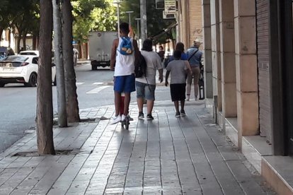 Un joven y un niño en patinete eléctrico sin casco y por la acera. 