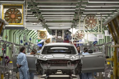 Diversos treballadors inspeccionen una carrosseria després de passar per la zona de pintura.