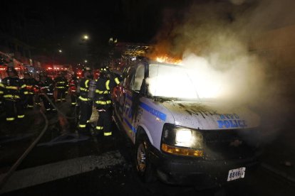 Els bombers de Nova York apaguen les flames d’un cotxe patrulla durant les protestes.