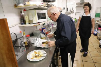 Un hostelero llena un táper con comida sobrante.