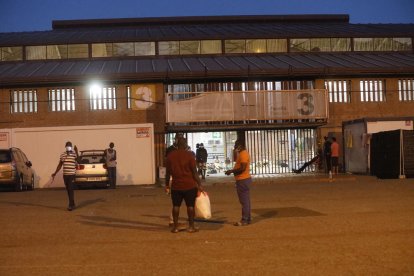 Varias personas conversan anoche frente a la entrada del pabellón 3 de la Fira donde pernoctan. 