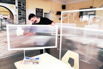 El dueño de un bar restaurante de Lleida prepara el interior del local con mamparas entre las mesas.