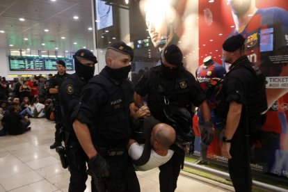 Agentes de los Mossos se llevan a uno de los concentrados en Sants mientras al fondo se ven todavía algunos de los que quedan sentados.