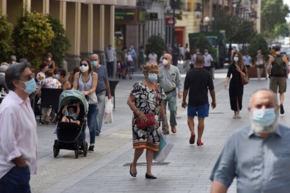 Varias personas pasean con la mascarilla puesta por una concurrida calle de Huesca. 