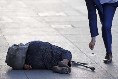 Una hombre echa una moneda a una mujer que practica la mendicidad.