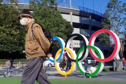 Un hombre protegido por una máscara pasa junto a los anillos olímpicos instalados en Tokio.