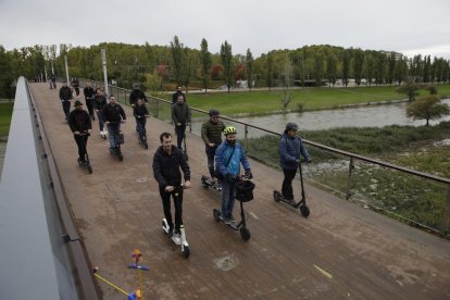 Usuaris de patinets elèctrics circulant per una passarel·la.