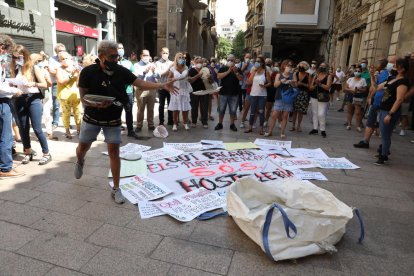 A la izquierda, tres personas desayunan en un banco del Eix tras pedir comida para llevar. A la derecha, un manifestante rompe platos frente al edificio del ayuntamiento. 