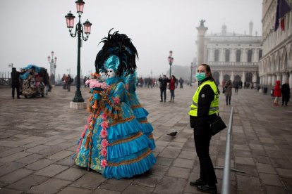 Gent disfressada ahir al Carnaval de Venècia, a prop de la plaça San Marco, al costat d’una guàrdia de seguretat amb màscara.