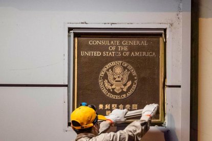 Un hombre quita la placa a la entrada del consulado de EEUU.