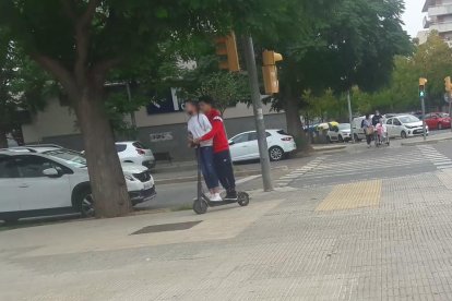 Dos jóvenes subidos en un patinete eléctrico y circulando por la acera en Lleida.