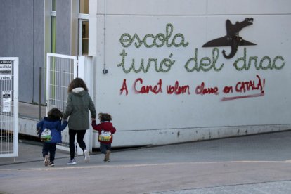 Una mare acompanya els seus fills a l'escola Turó del Drac de Canet de Mar. Una pintada reclama l'ensenyament en català a la façana del centre.