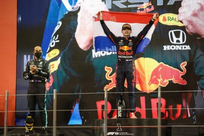 Max Verstappen festeja en el podio su primer título mundial de Fórmula Uno, con Lewis Hamilton a su lado aplaudiendo.