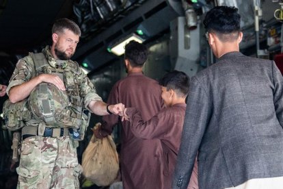 Un militar británico saluda a un menor afgano a punto de embarcar en un avión que le sacará de Kabul.