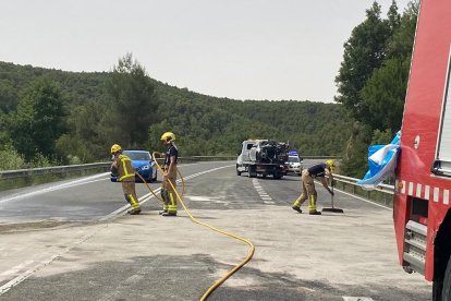 Bombers netejant la carretera, que va estar unes tres hores tallada, i al fons un dels turismes implicats.