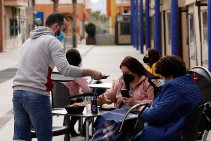 Un cambrer serveix una comanda a unes clientes en una terrassa.