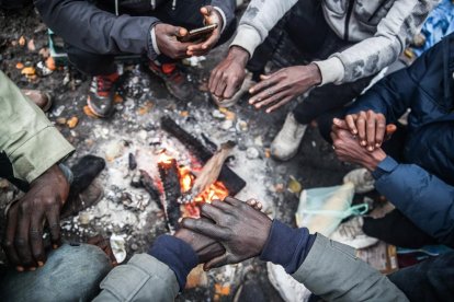 Un grup de migrants s’escalfa en un campament a Calais.