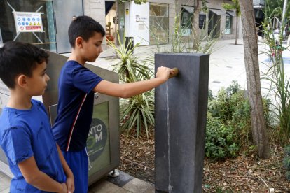 Dos nens obrint una font d'aigua en una plaça de Mollerussa.