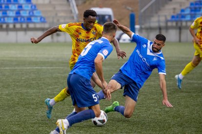 El davanter del Lleida Alpha Bagayoko intenta avançar amb la pilota controlada entre dos jugadors del Badalona.