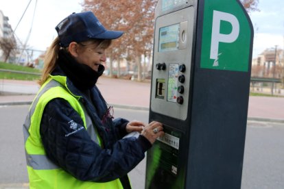 Una controladora de la zona blava de Lleida canvia l'adhesiu amb el nom de l'antiga concessionària pel de l'EMAU en un parquímetre.