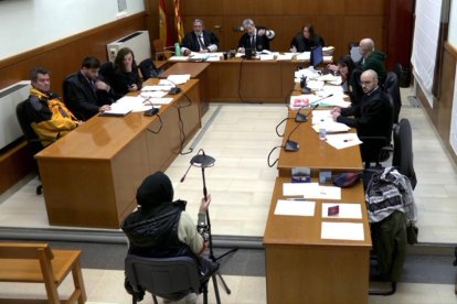 Imatge extreta de senyal de vídeo de la filla gran de la denunciant en el judici per racisme contra un conductor d'autobús de TMB, assegut a l'esquerra.