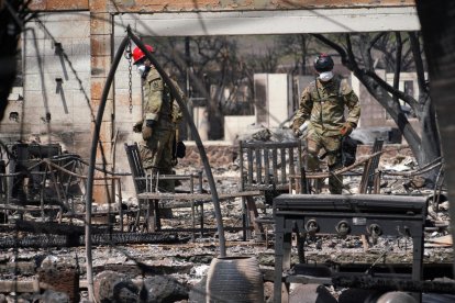 Dos soldados inspeccionan los restos de una vivienda arrasada por el fuego.