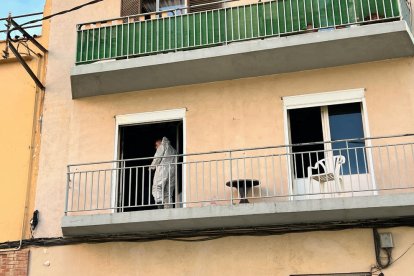 Un agent de la policia científica surt del balcó del pis incendiat a Figueres en la investigació de les causes del foc.