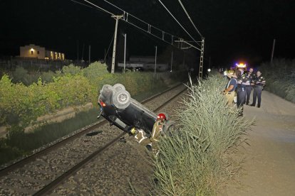 El cotxe bolcat sobre la via del tren i els serveis d’emergències que es van desplaçar fins al lloc.